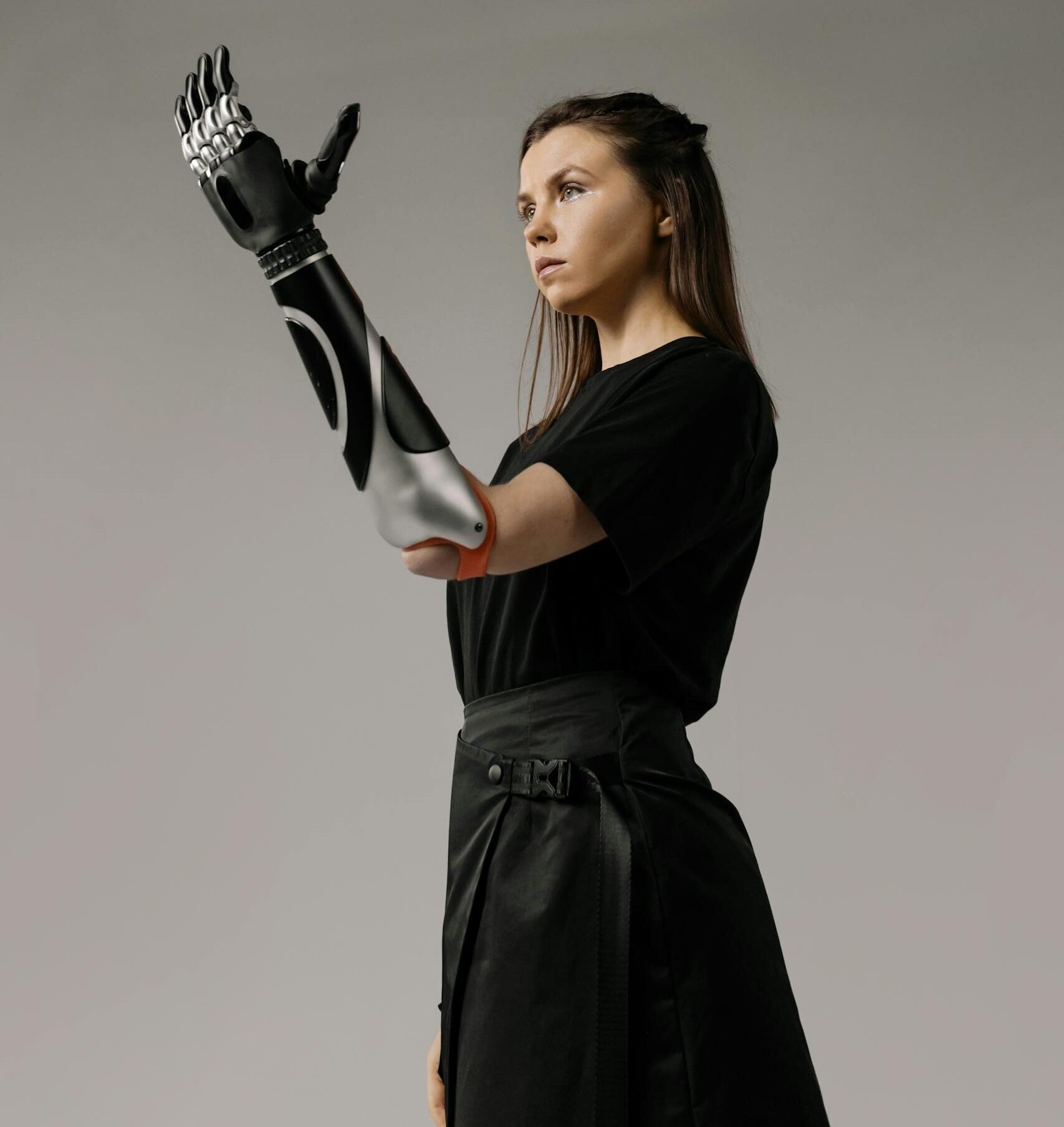 Caucasian woman in black outfit wearing advanced prosthetic arm, studio close-up.