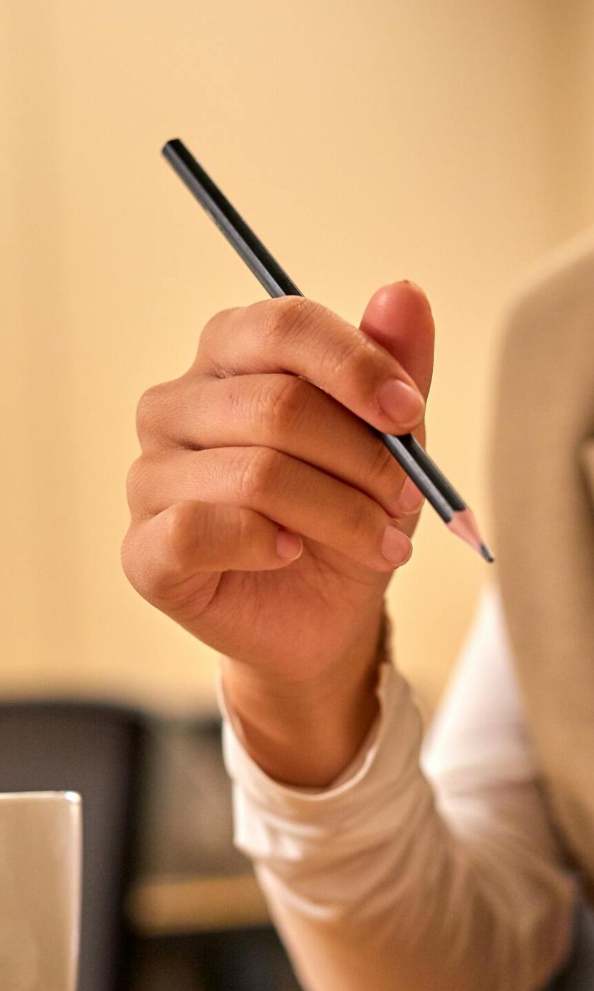 A person in an office writing in a notebook with a pencil, coffee cup in view.