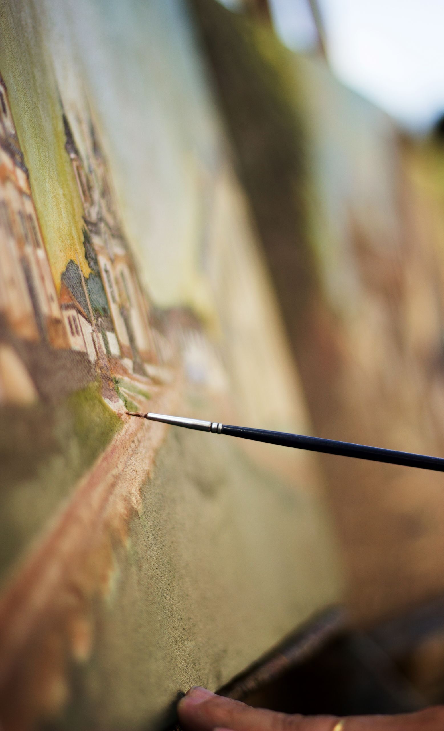 An artist's hand skillfully paints on a canvas outdoors, capturing a vibrant scenery.